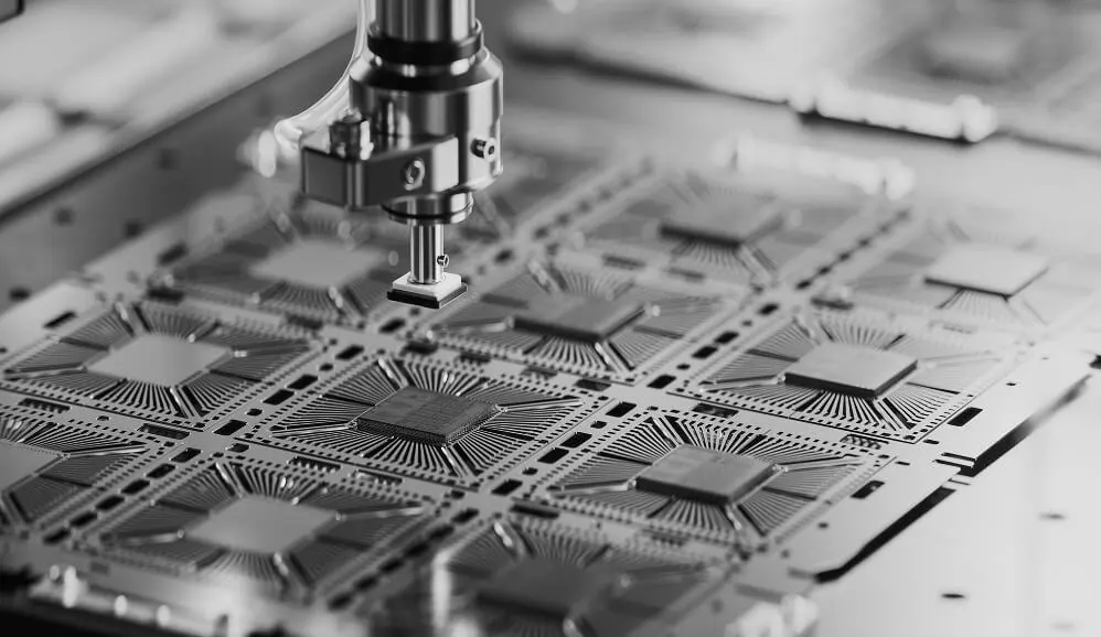 A robotic arm places a microchip onto a grid of semiconductor chips during automated manufacturing.