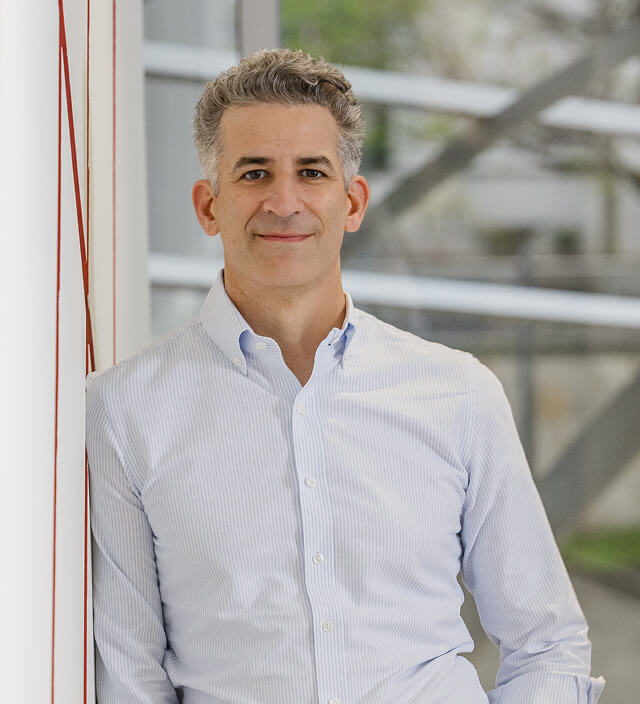 Billy Man, a Quandrant team leader, smiling in a light blue striped button-down shirt against a modern glass building